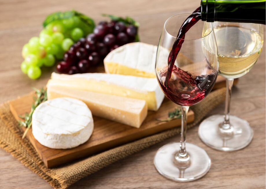 A cheeseboard featuring a variety of cheeses paired with a glass of white wine and a glass of red wine.