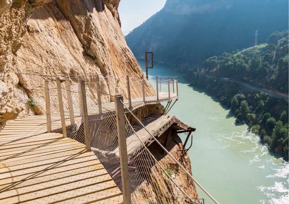 Elevated walkway along the cliffs of Caminito del Rey with hikers and dramatic canyon views.
