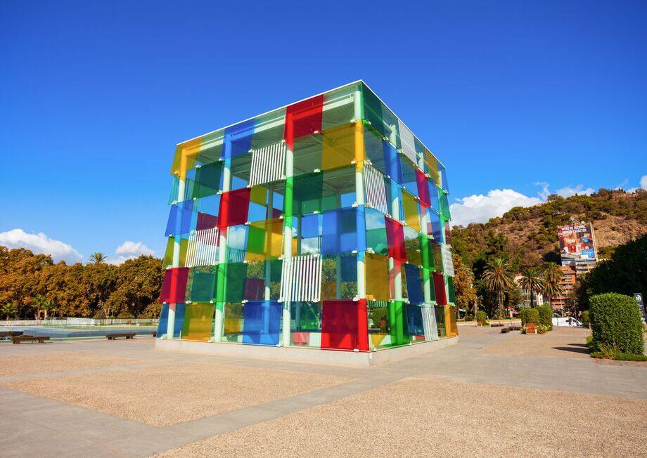 Colorful glass cube of Centre Pompidou Málaga with modern art visitors near the waterfront.